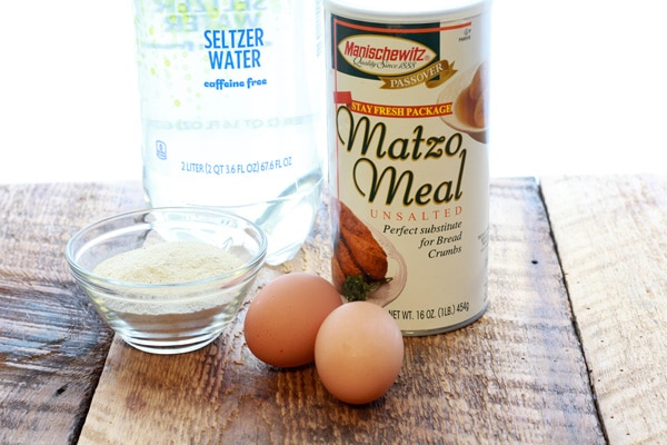 A box of Manischewitz matzo meal, two eggs, and seltzer water placed on top of a wooden board.