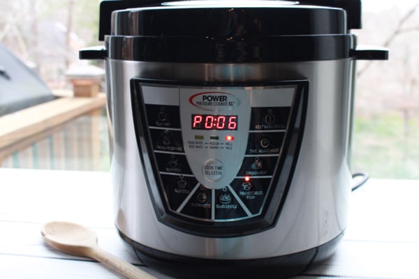 A pressure cooker instant pot placed on a white board with a wooden spoon on the side.