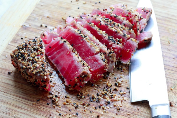 Slices of sesame seared tuna on a wooden cutting board with a chef's knife on the side.