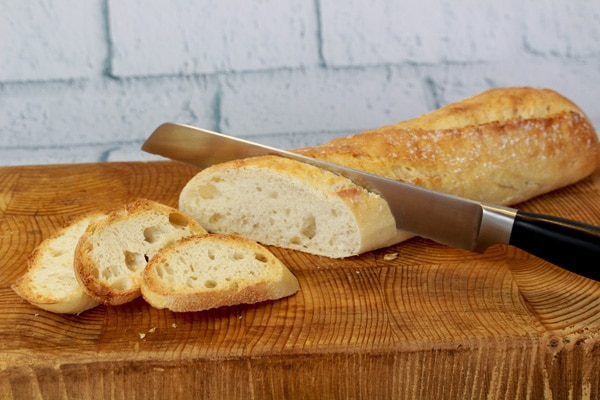 French bread being sliced on a cutting board with a bread knife.