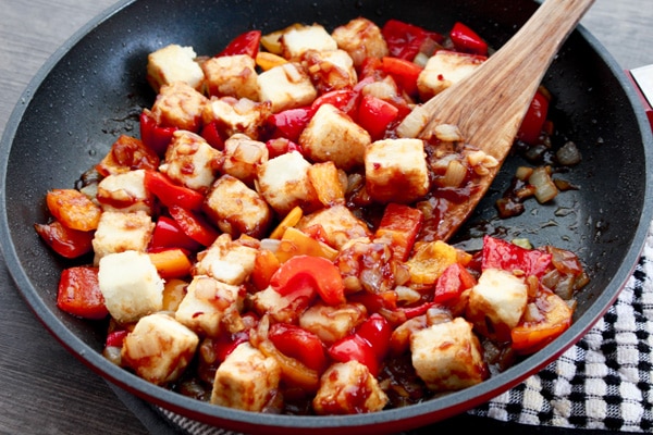 crispy tofu cubes in a skillet tossed in a sweet and sour sauce.