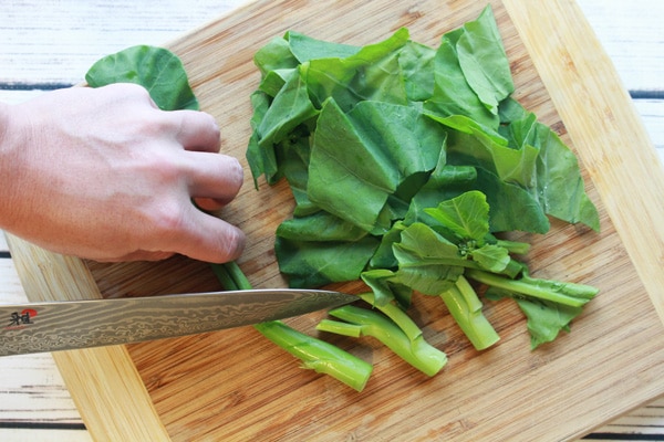 chopping Chinese broccoli on a wooden cutting board.