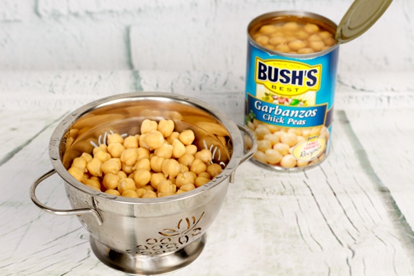 Chickpeas in a silver strainer and chickpeas in a can of Bush's Best.