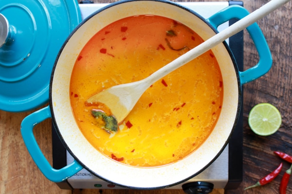 Singapore laksa broth in a blue Dutch oven with a wooden spoon.