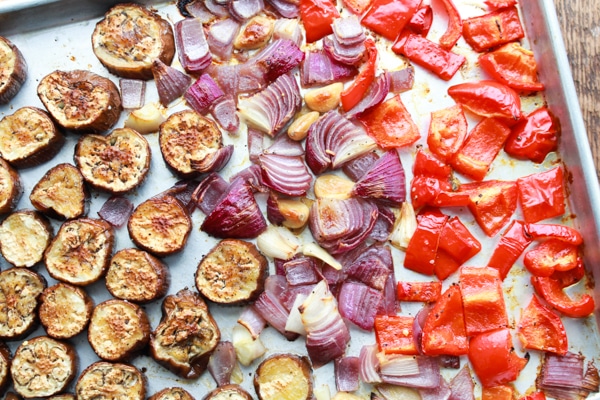 roasted sliced eggplant, red onions, and red bell peppers on a baking sheet.