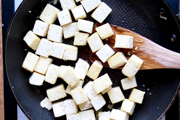tofu cubes in a frying pan with a wooden spatula.