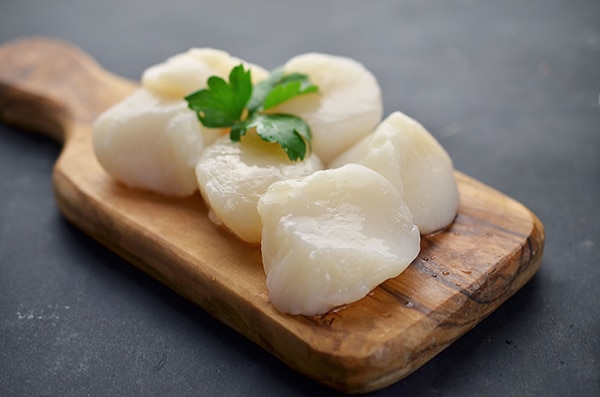 Raw scallops with herbs on a wooden cutting board.