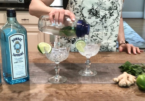 Pouring minty ginger fizz cocktail into a crystal glass with Bombay gin on the side