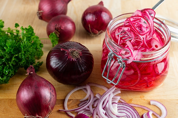 homemade pickled sliced red onions in a canning jar with fresh onions on the side