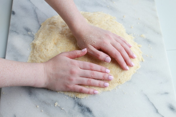A woman's hands kneading Chinese almond cookie dough on a pastry board on top of a marble suirface.