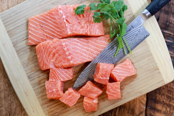 raw salmon being cubed on cutting board with chef's knife and cilantro sprigs