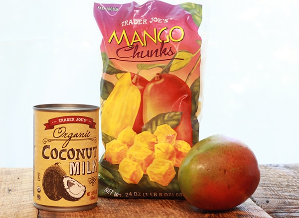 ingredients for mango coconut sorbet on a wood board including a package of frozen mango chunks, can of coconut milk, and a whole mango