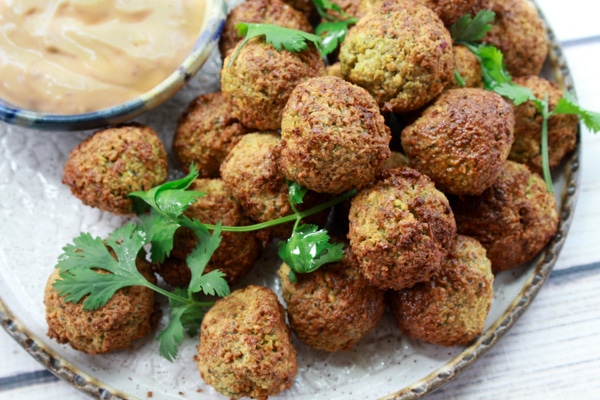 air-fried falafel balls on a white plate with a side of spicy aioli dipping sauce on top of a white wooden board