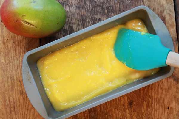 mango coconut sorbet in a loaf pan with a rubber spatula and whole mango on the side