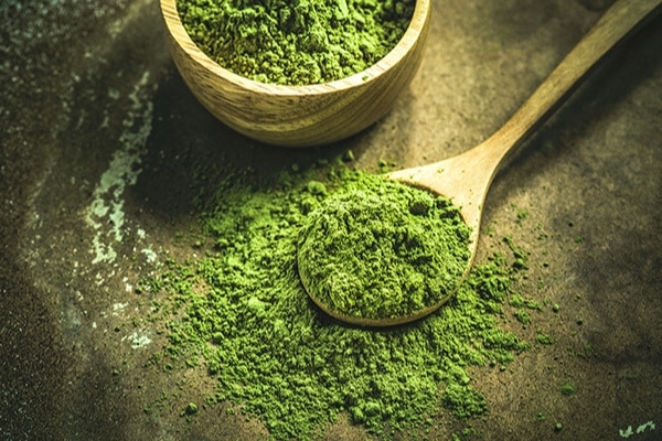 matcha powder in a wooden bowl and in a wooden spoon