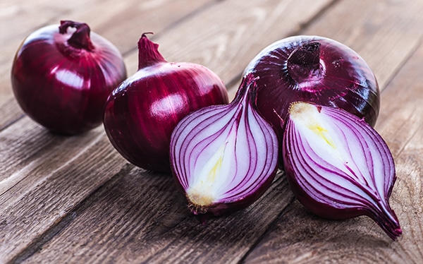 whole and halved red onions on rustic wooden board