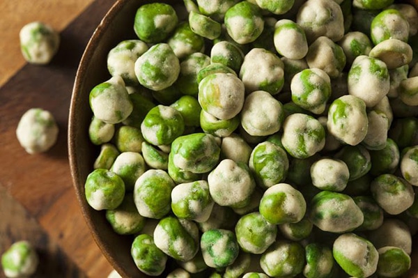 a bowl of wasabi peas on a wooden board