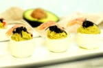 avocado deviled eggs topped with fresh shrimp and caviar stacked on a white plate