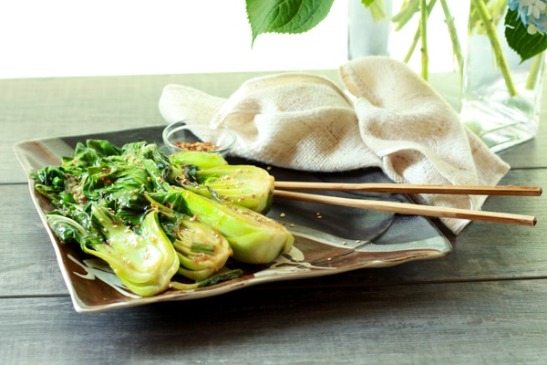 stir-fried baby bok choy on a brown serving plate with chopsticks on the side on top of a wooden board