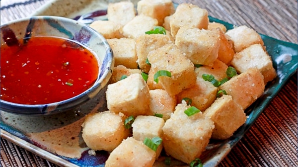 Cubes of crispy tofu on a green plate with a side of sweet chili dipping sauce.