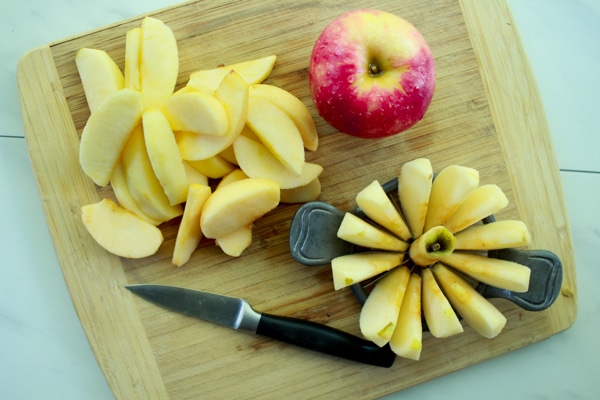 slices of apples on a cutting board with a pairing knife, apple cutter, and whole apple