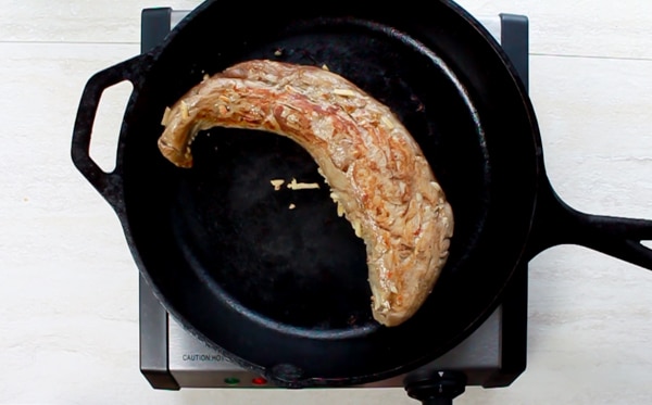 pork tenderloin being seared in a black cast iron skillet on top of an electric stove