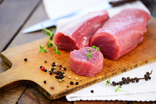 raw pork tenderloins on a wooden cutting board with a knife in the background