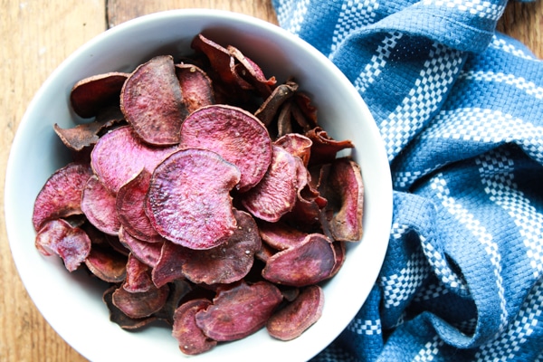 baked purple sweet potato chips in a white bowl with a blue napkin on the side