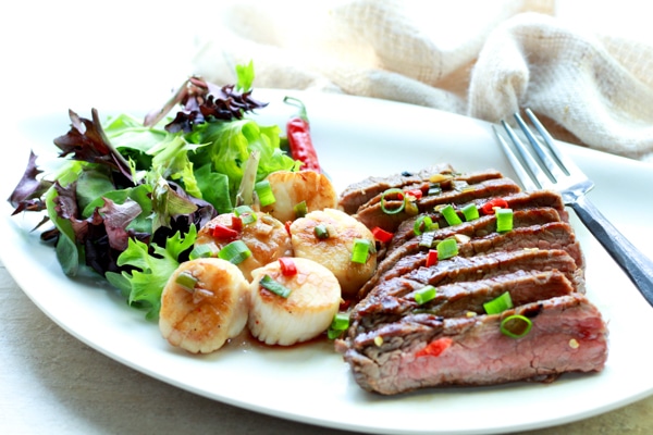 grilled flank steak slices and seared scallops on a white plate with a green salad on the side