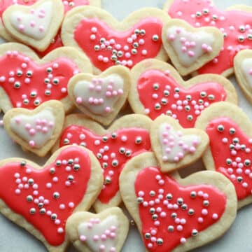 Heart-shaped sugar cookies in various sizes with pink and white glaze and decorative sprinkles stacked on top of a marble surface.