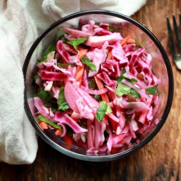 pickled vegetables in a glass bowl with a napkin and fork on the side on top of a wooden board