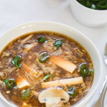 hot and sour soup in a white bowl with chopped green onions in the background