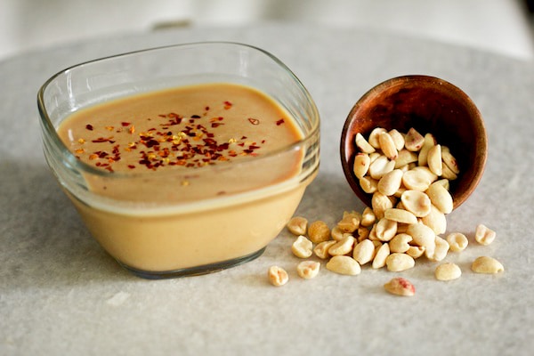 Asian peanut dipping sauce in a glass bowl with peanuts spilling out of a bowl on the side.