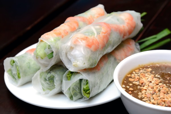 Fresh Vietnamese shrimp spring rolls on a round white plate with a white bowl of peanut sauce on the side
