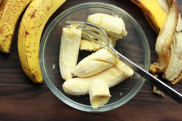 slices of banana in a glass bowl with ripe bananas on the side