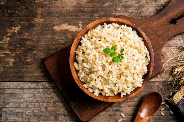 Bowl of cooked brown rice in a wooden bowl on a wooden board