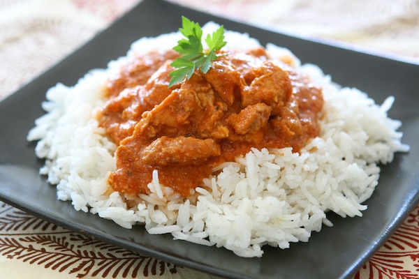 chicken tikka masala on a bed of white rice on a black square plate