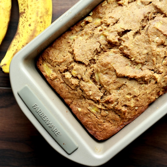 banana bread in a loaf pan with ripe bananas on the side