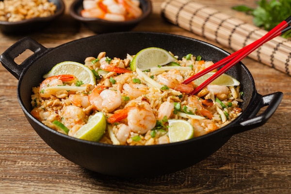 shrimp fried rice in a large black wok with red chopsticks on a wooden board