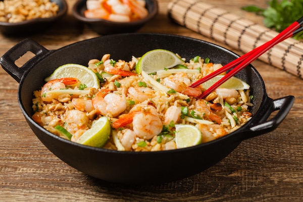 Shrimp fried rice in a large black wok with red chopsticks on top of a wooden board.