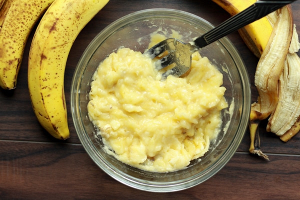 mashed bananas in a glass bowl with ripe bananas on the side