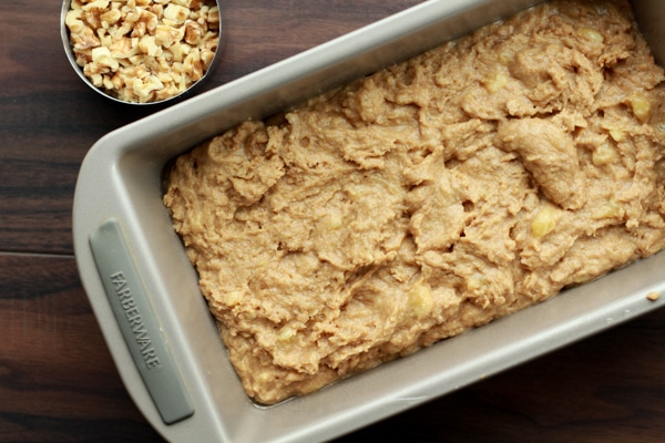banana bread mixture in a loaf pan with chopped walnuts on the side