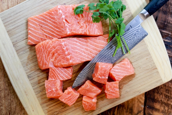 Fresh sushi-grade salmon on a wooden cutting board with a chefs knife.