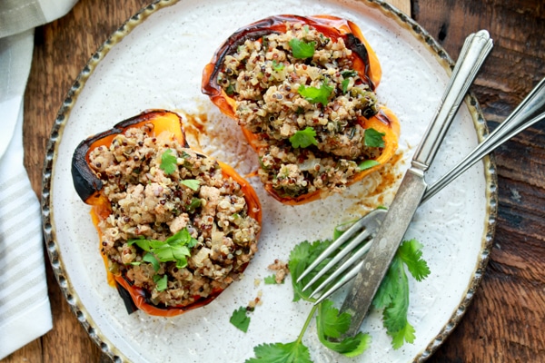 stuffed yellow bell peppers with turkey and quinoa on a white plate with a knife and fork on top of a wooden board