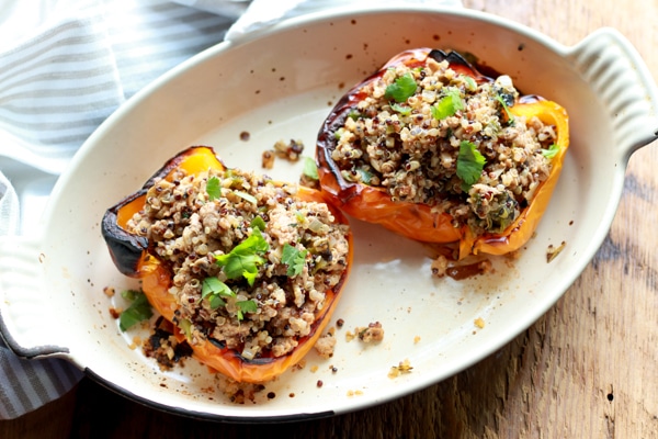 stuffed yellow bell peppers with turkey and quinoa in a white oval dish on a wooden board