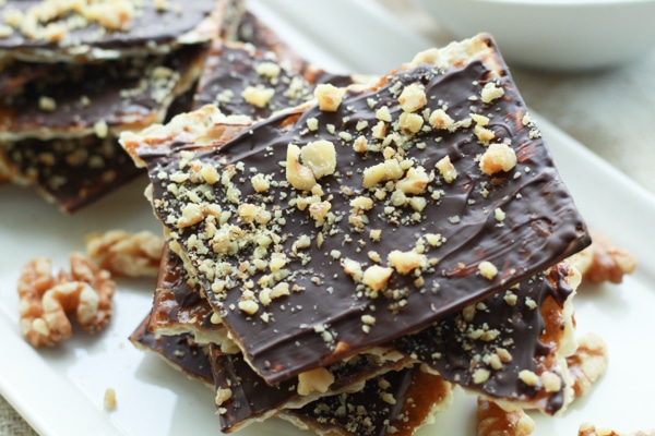 chocolate covered matzo on a white plate with sprinkles of walnuts on top