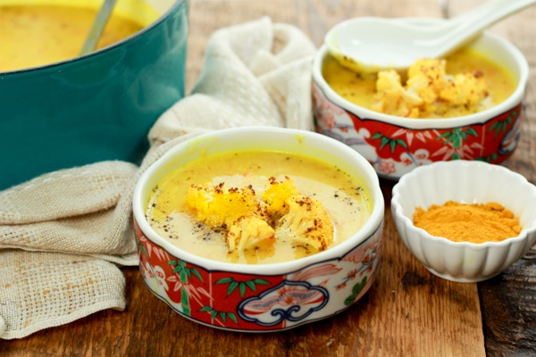 vibrant cauliflower soup in two bowls on a wooden board with turmeric powder on the side