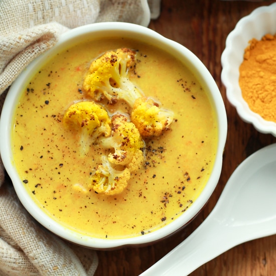 vibrant cauliflower soup in a white bowl with a white spoon and turmeric powder on the side