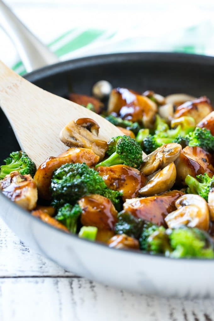 chicken and broccoli stir fry in a large wok on a white wooden board