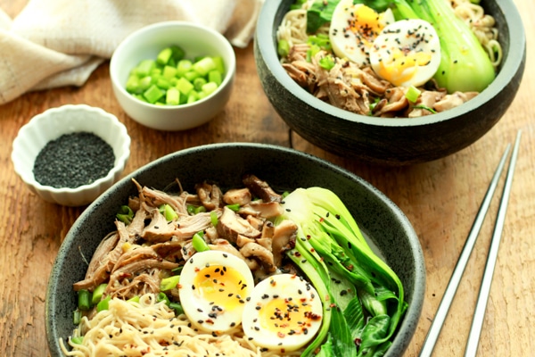 two bowls of pulled pork ramen bowls on a wooden board with chopsticks on the side